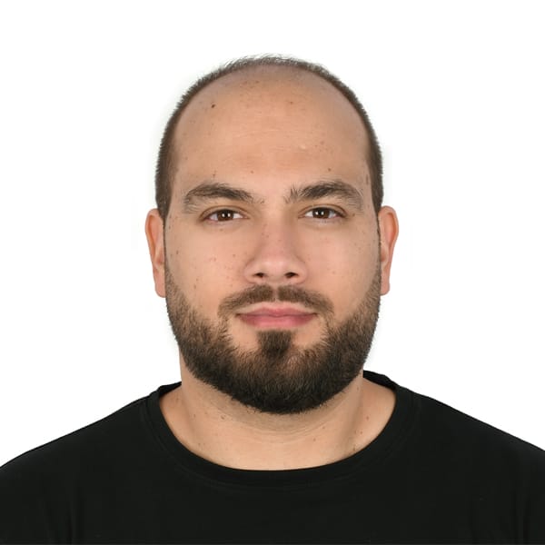 A person with a shaved head and full beard is wearing a black crew-neck t-shirt. They have a neutral expression and are facing directly towards the camera against a plain white background.