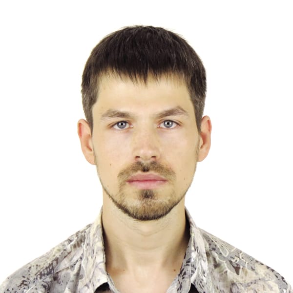 A man with short dark hair and a beard is facing forward with a neutral expression. He is wearing a patterned button-up shirt. The background is plain white.